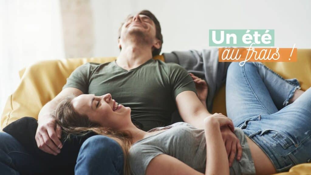 Jeune couple, en train de se relaxer, en t-shirt sur un canapé. Ce qui les fait sourire : la climatisation et les économies d'énergie.