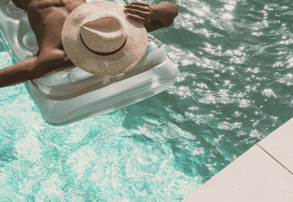 Un homme avec un chapeau sur le visage allongé sur un matelat gonflable dans une piscine