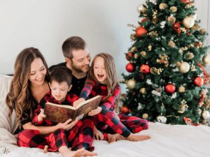 Une famille avec une femme, un homme, leur fils et leur fille. Il sont habillés en pyjama de noël à carreau et sont assis sur un lit en lisant un livre. Un sapin de Noël est en arrière plan