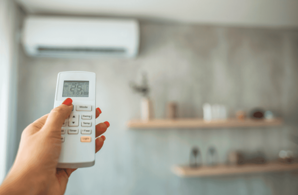 Une main de femme avec une télécommande de climatisation dans la main qui point la climatisation