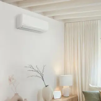Unité intérieure de climatisation murale blanche installée en hauteur dans un salon lumineux avec rideaux clairs et mobilier en bois.